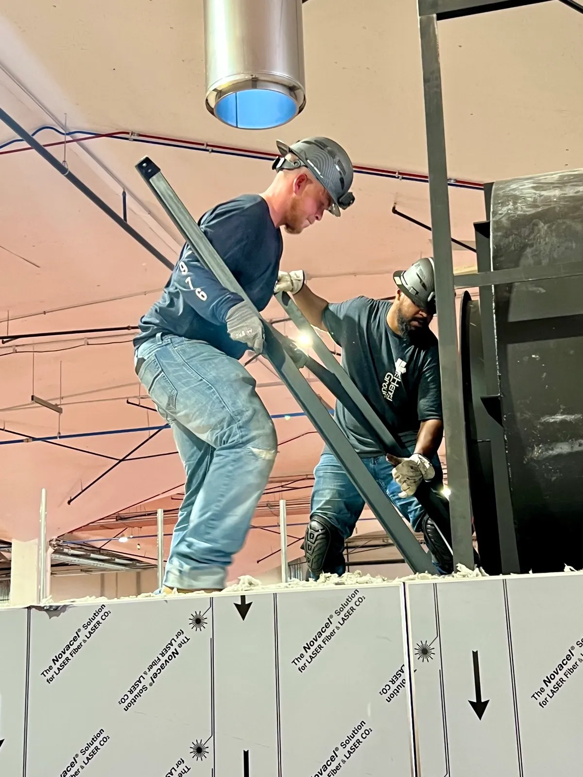 Two Henry Group crew members standing on top of an industrial oven maneuver a steel frame member into place during installation.