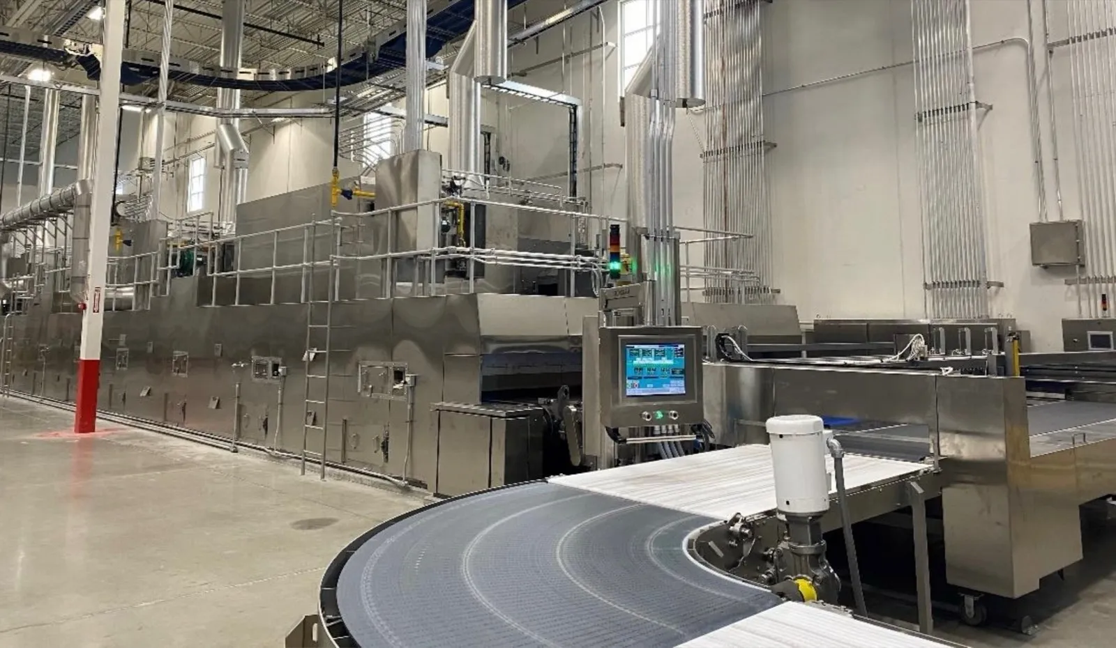 A finished bakery oven line with its HMI control panel and a curving product conveyor running out of the discharge end.